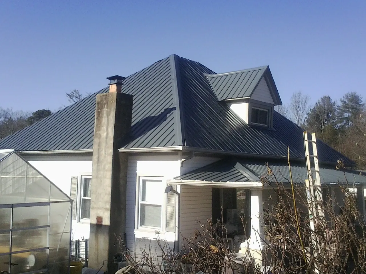 Dark blue standing seam metal roof on a white farmhouse with dormer — Slate & Tile Roof Repair by Roofing Brothers in Lindale