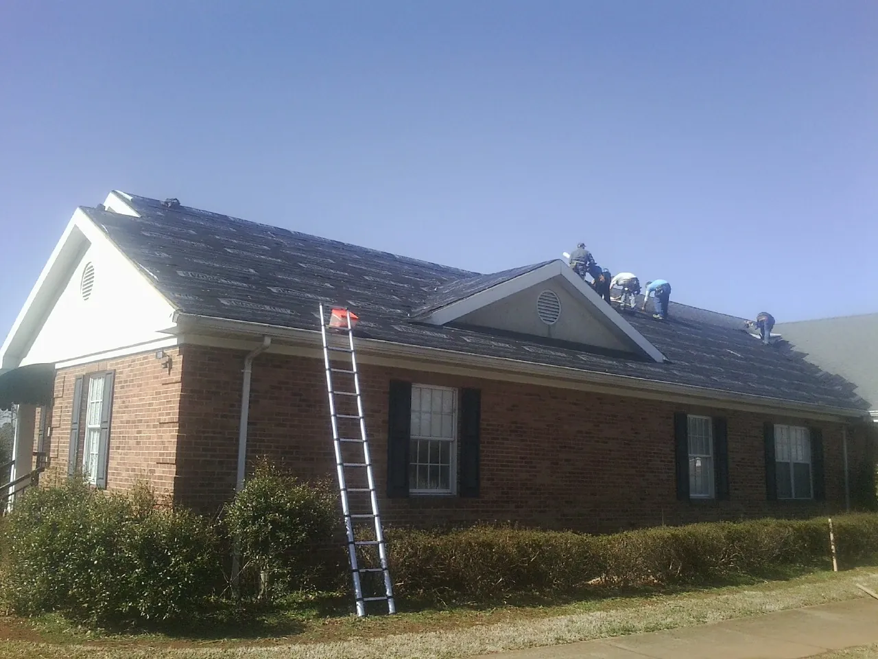 Crew tearing shingles off a brick ranch roof with a ladder set — Metal Roof Repair work by our crew in Lindale