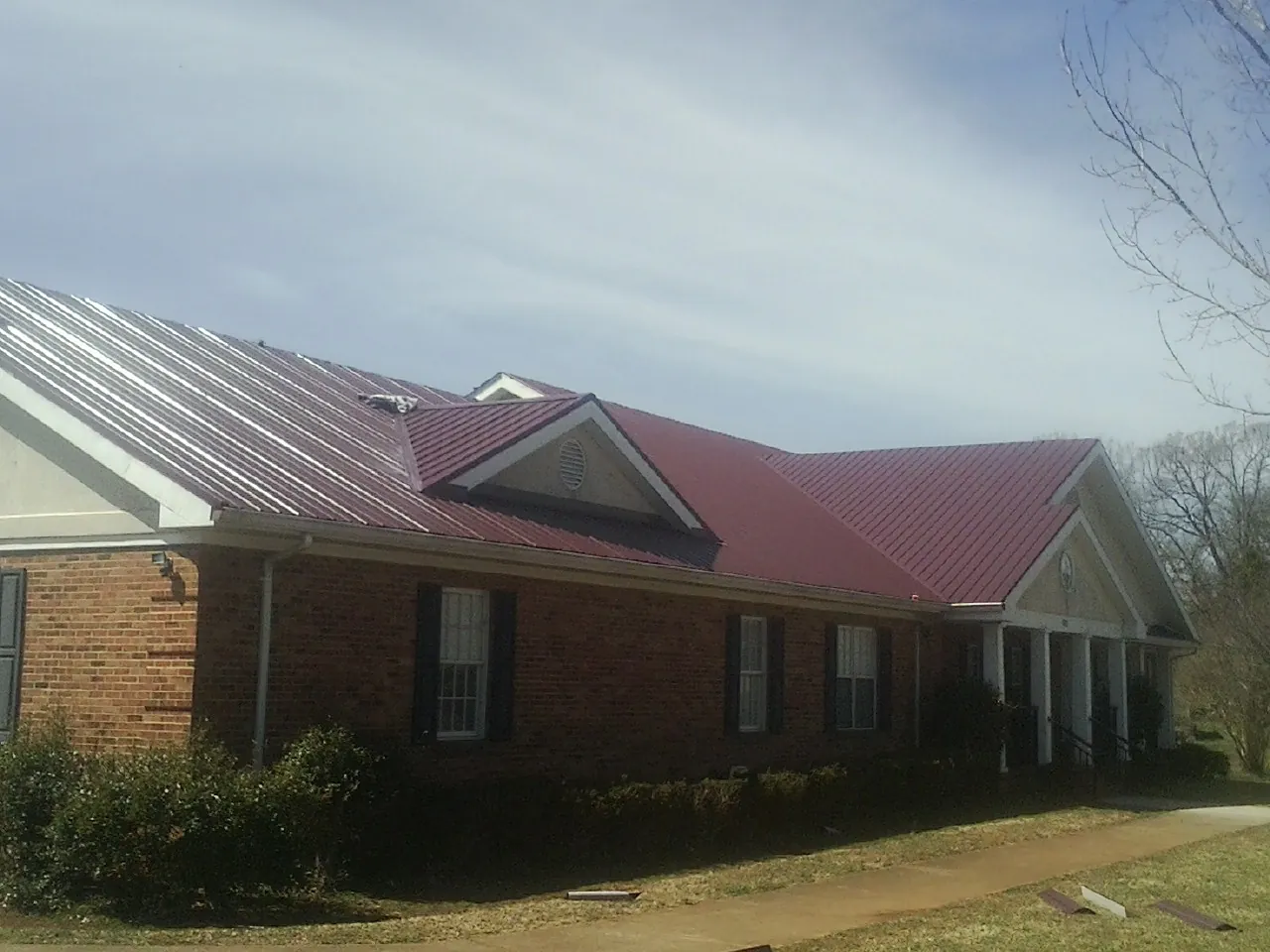 Red metal roof with gabled entries on a long brick building, from a Hail Damage Roof Repair job in Lindale