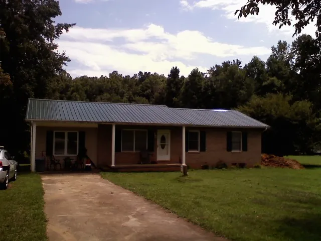 Dark green metal roof on a brick ranch with a covered porch in Lindale
